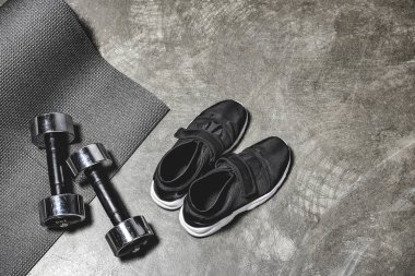 top view of sporting shoes with yoga mat and dumbbells lying on concrete surface
