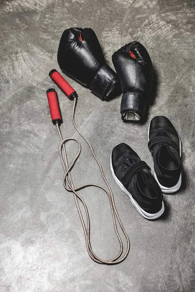 sporting shoes with jumping rope and boxing gloves on concrete surface