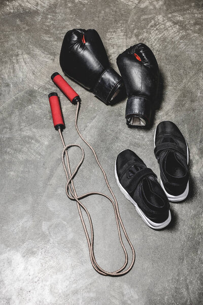 спортивная обувь с скакалкой и боксёрскими перчатками на бетонной поверхности
