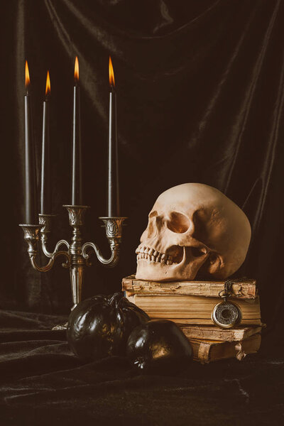 halloween skull on ancient books with black pumpkin, apple and candles on black cloth