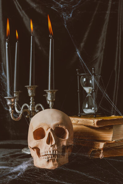 halloween skull, ancient books with hourglass and candles on black cloth