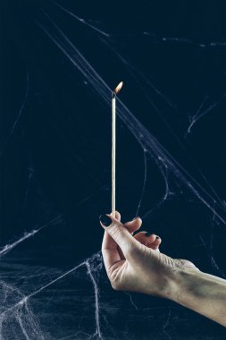 cropped view of gothic woman holding big flaming match in darkness with spider web clipart