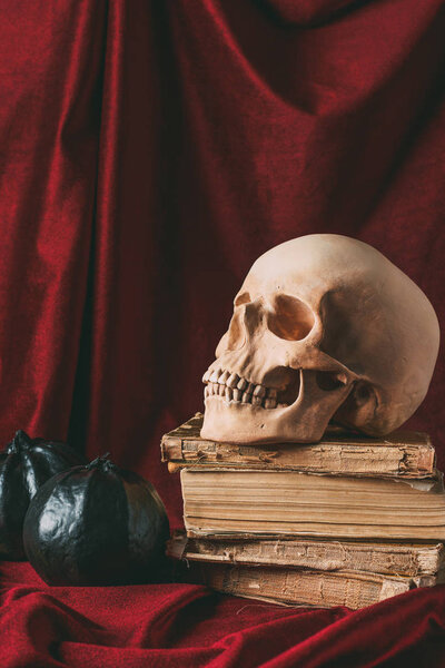halloween skull on ancient books with black pumpkins on red cloth