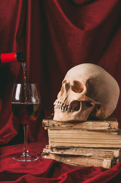 red wine, halloween skull on ancient books on red cloth