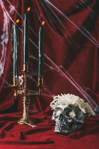 银色头骨与花和烛台用蜡烛在红色布料与蜘蛛网 — 图库照片