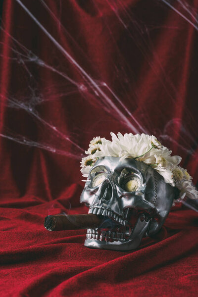 silver skull with flowers smoking cigar on red cloth with spider web 