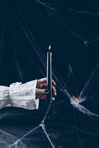 cropped view of scary woman holding black candle in darkness with spider web