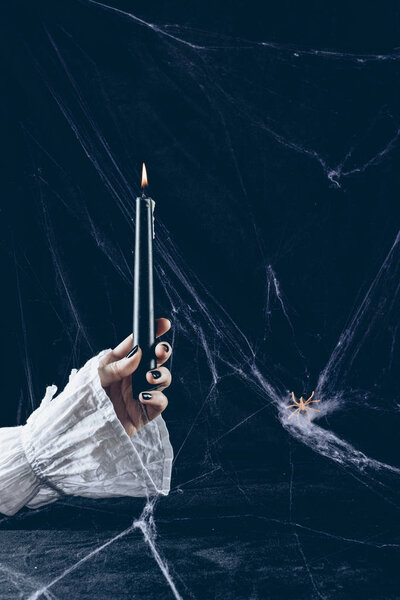 partial view of creepy woman holding black candle in darkness with spider web