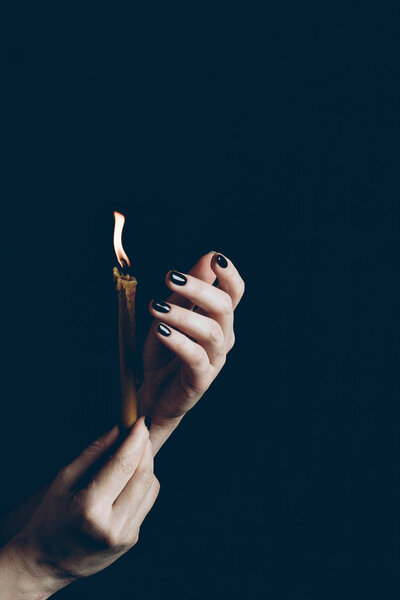 cropped view of gothic woman holding flaming candle isolated on black