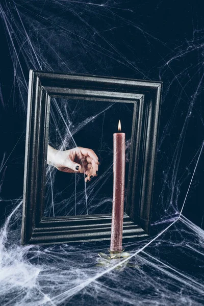 cropped view of mystic hand taking candle from mirror frame with scary spider web around