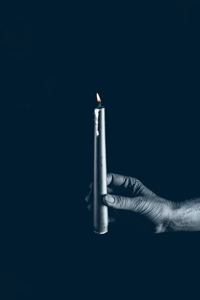 partial view of demon holding flaming candle in black hand, isolated on black