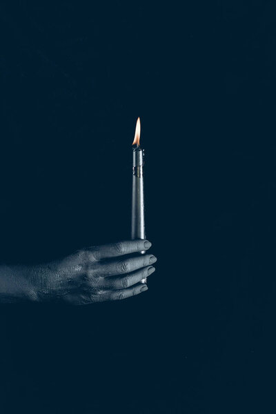 cropped view of black hand with flaming candle, isolated on black
