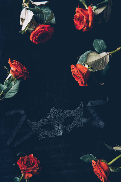 top view of lace mask and beautiful red roses on black