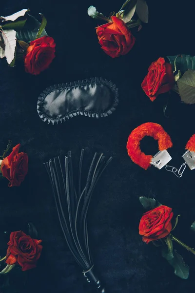 黑色面具 皮革鞭和红色蓬松的手铐与玫瑰的顶部视图 — 图库照片