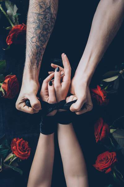 partial view of man tying female hands with black ribbon 