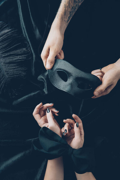 cropped shot of woman with tied hands and man holding black mask 