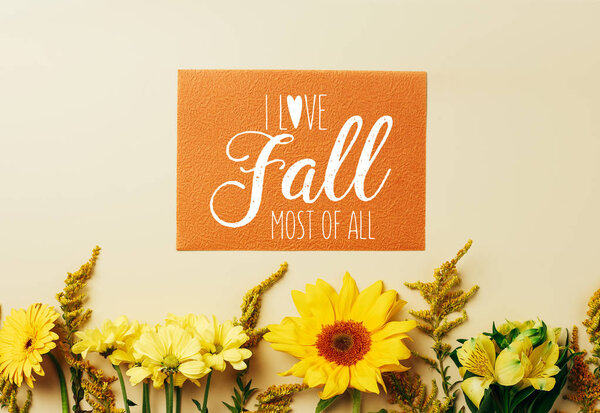 flat lay with beautiful flowers and orange card with "I love fall most of all" inspiration arrangement on beige backdrop