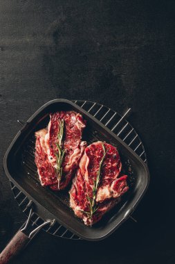 top view of raw steaks with rosemary on grill pan in kitchen clipart