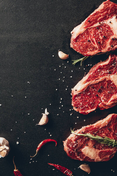 top view of raw meat steaks and garlic with chili peppers on tabletop in kitchen