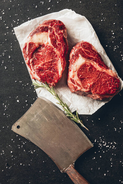 top view of raw meat steaks, spices and cleaver on tabletop in kitchen