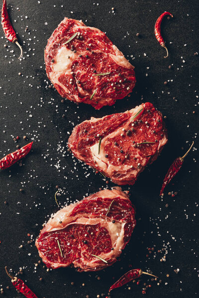 top view of raw steaks and scattered spices on table in kitchen