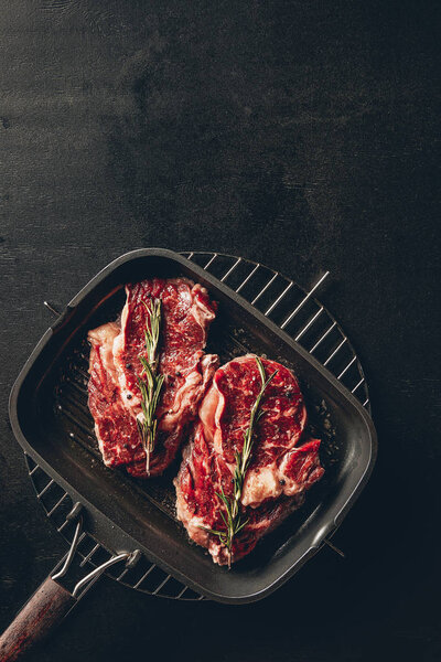 top view of raw steaks with rosemary on grill pan in kitchen