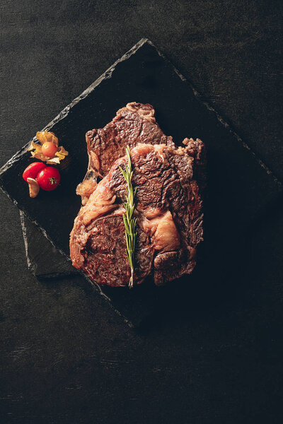 top view of cooked steaks with rosemary and cherry tomato on cutting boards in kitchen