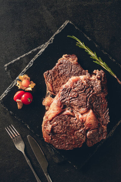 elevated view of tasty roasted steaks with rosemary and berry on cutting boards in kitchen