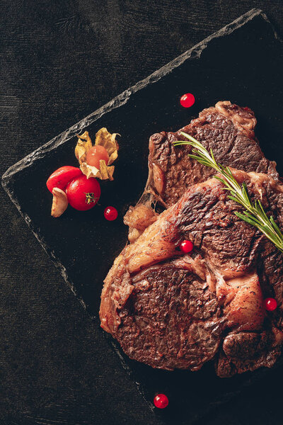 elevated view of appetizing steaks with rosemary and berries on cutting boards in kitchen