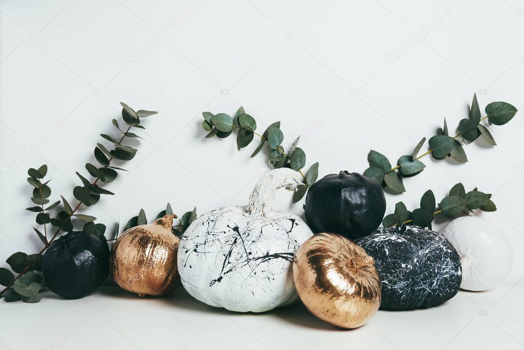 still life with golden, black and white painted pumpkins with eucalyptus branches, halloween decoration