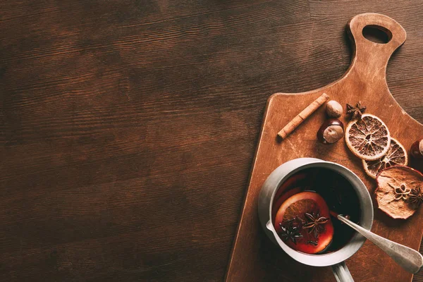 top view of homemade hot mulled wine with spices on cutting board on wooden background