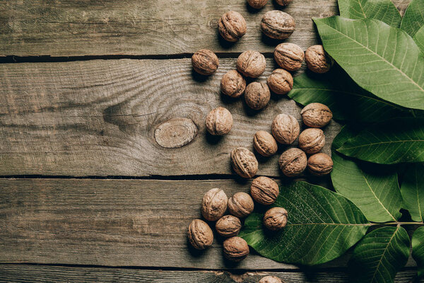 top view of whole natural walnuts and green leaves on wooden table