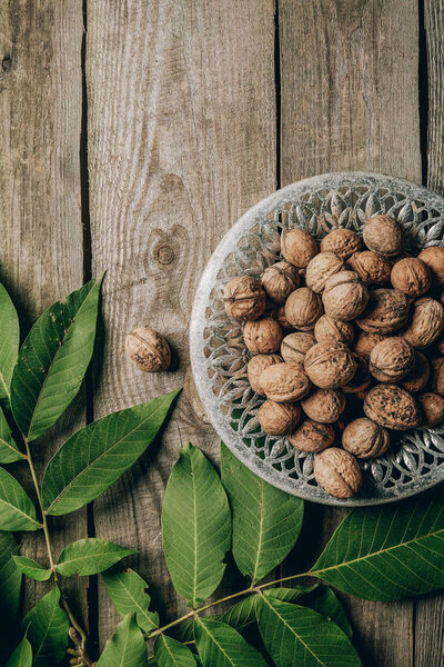 top view of tasty healthy walnuts on plate and green leaves on wooden table 