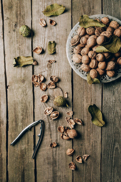 top view of whole walnuts on plate, nutshells and nutcracker on wooden table