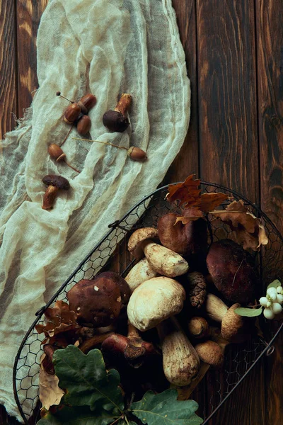 top view of fresh picked various edible mushrooms in basket on wooden table