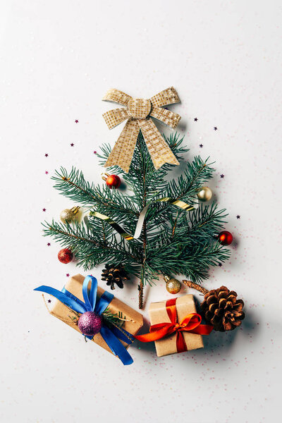 top view of green pine branch decorated as festive christmas tree with gifts and bow on white background
