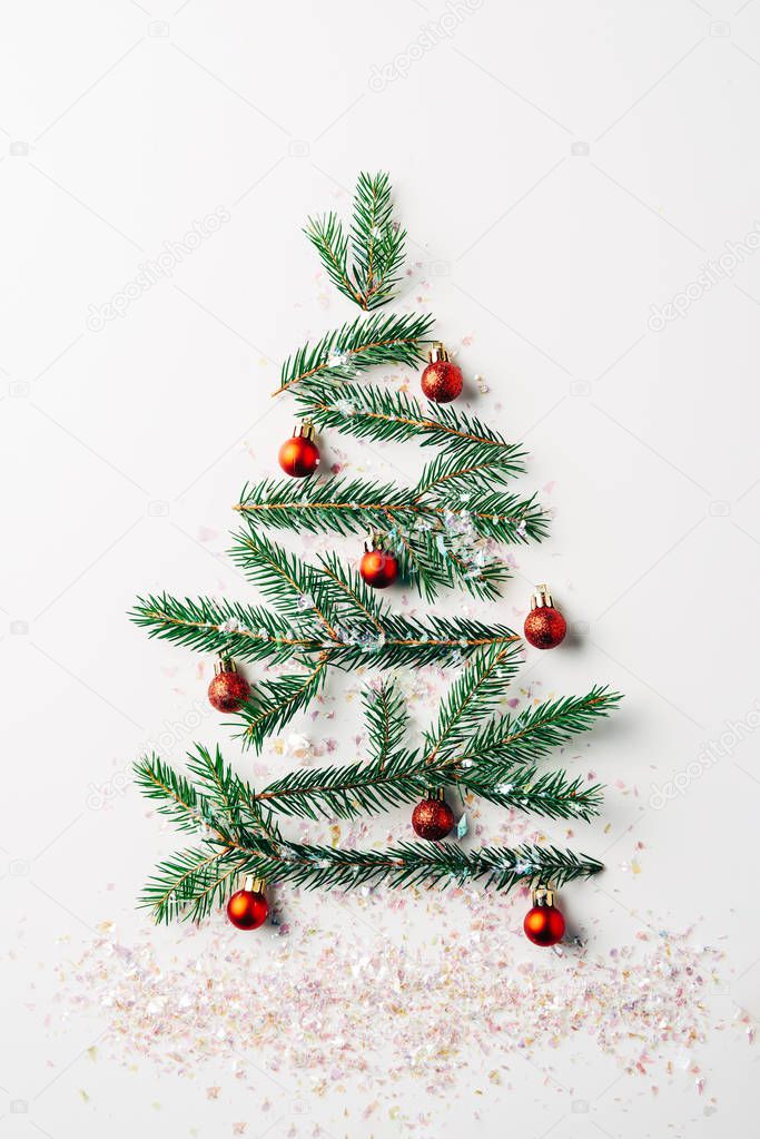 top view of green pine branch decorated as festive christmas tree with glitters on white background