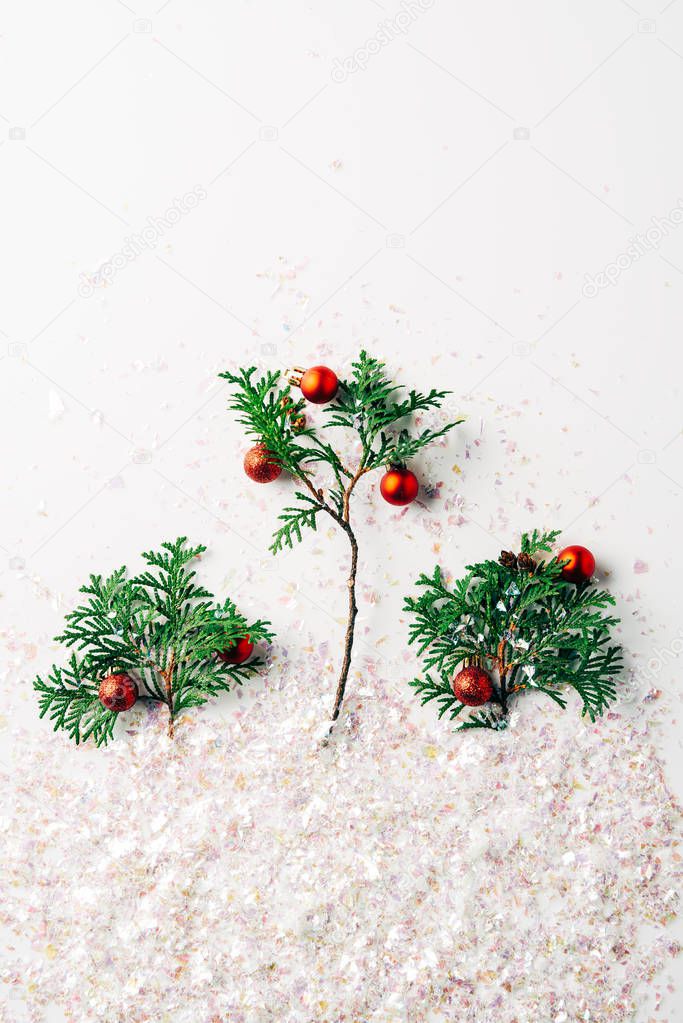 flat lay with pine tree branches decorated with christmas balls with glitters on white surface