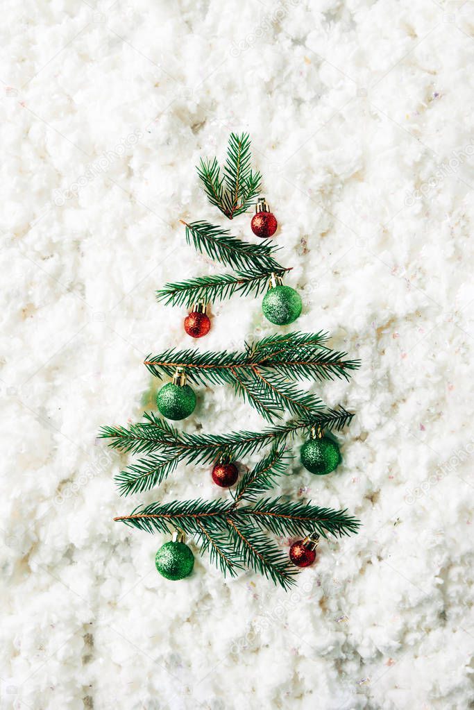 top view of green pine branches with christmas balls arranged in festive christmas tree on white cotton wool backdrop