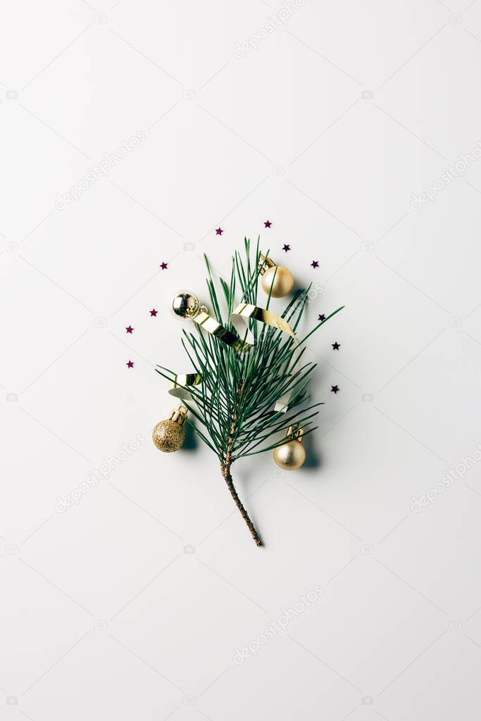 top view of little pine tree branch with ribbon and christmas toys on white surface
