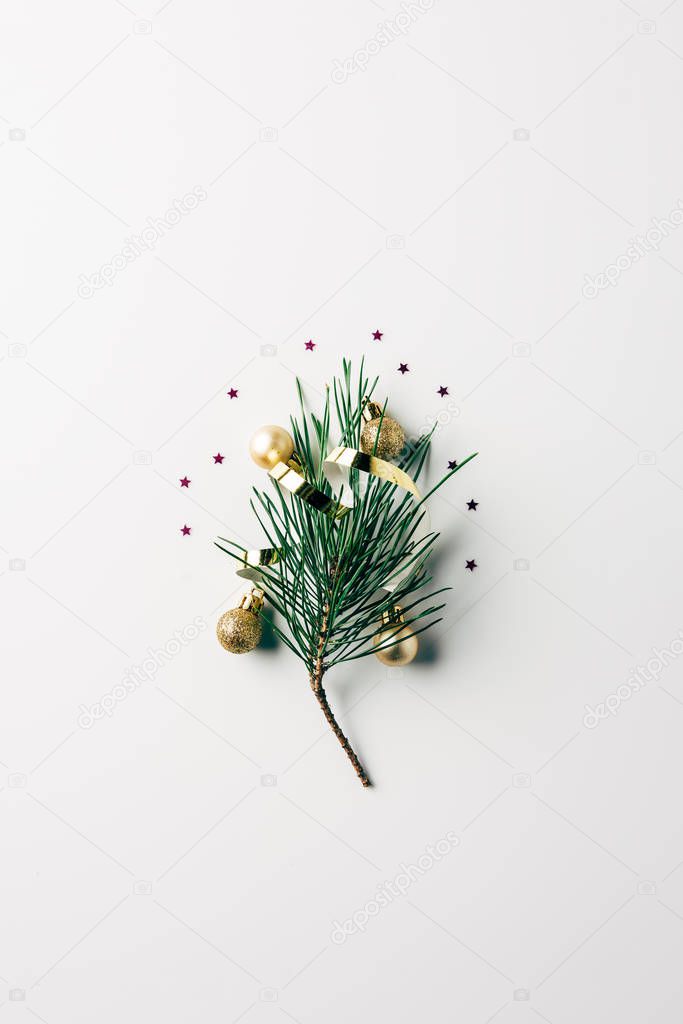 top view of little pine tree branch with ribbon and christmas balls on white surface