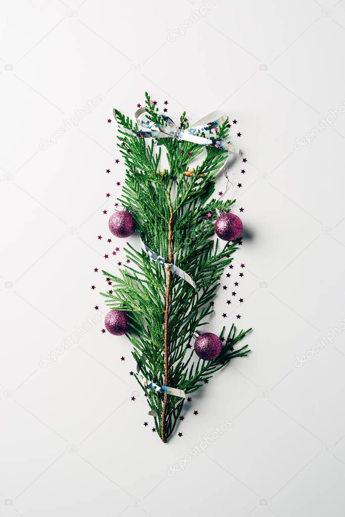 top view of green pine branch decorated with christmas toys and ribbon as christmas tree on white backdrop
