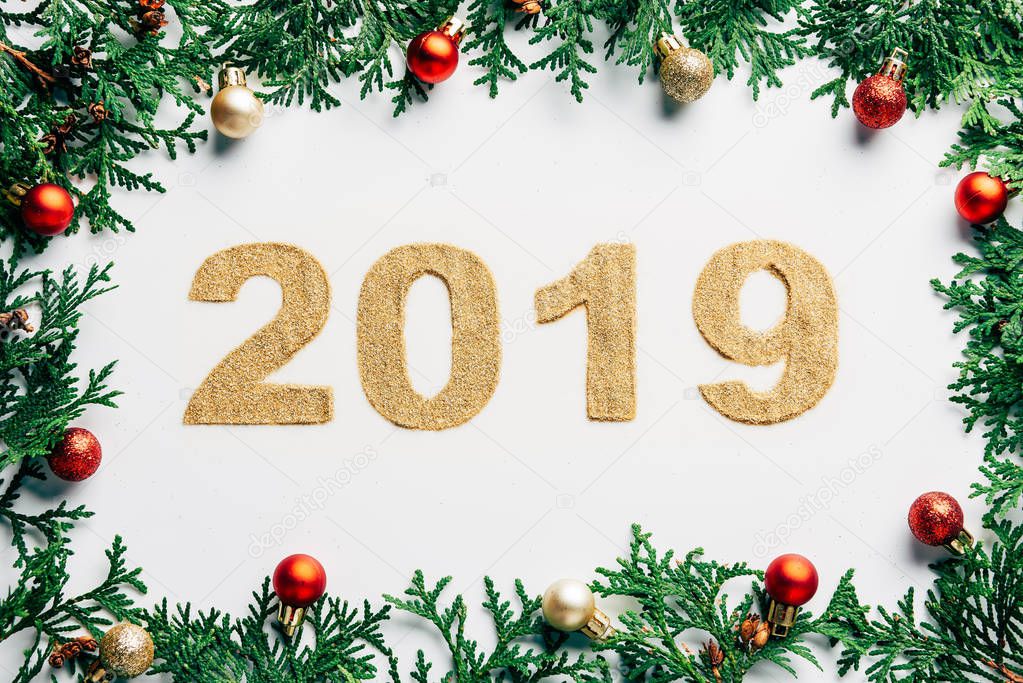 top view of 2019 year sign, pine tree branches and christmas balls on white background
