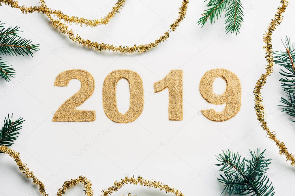 top view of 2019 year sign made of golden glitters, garlands and pine branches on white backdrop