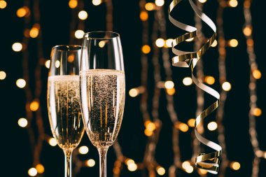champagne in glasses and ribbons on garland light background, christmas concept clipart
