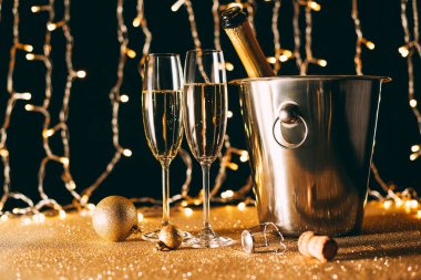 two glasses and champagne bottle in bucket on garland light background, christmas concept clipart