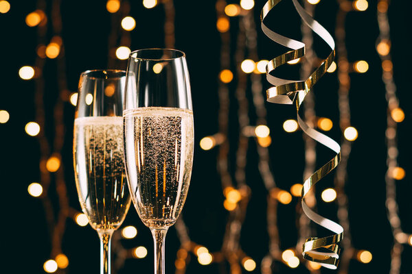 champagne in glasses and ribbons on garland light background, christmas concept