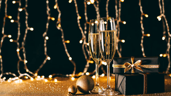 glasses of champagne, baubles and gifts on garland light background, christmas concept
