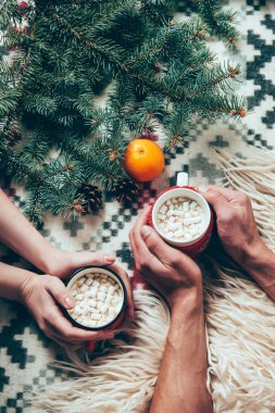 cropped shot of couple holding cups of cocoa hot drinks at background with pine tree branches and tangerine  clipart