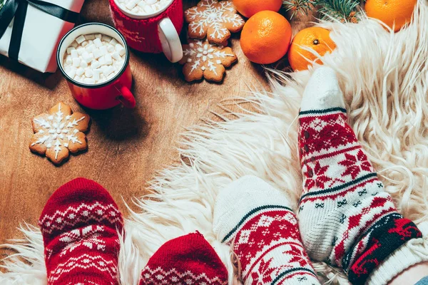 cropped shot of women in winter socks at background with cups of cocoa with marshmallows